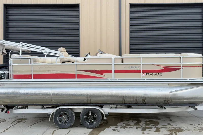 The Image of 2008 Harris Super Sunliner 220 pontoon boat on trailer, beige and red design, parked by garage. - 1