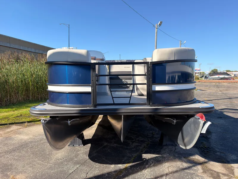 Slide: The Image of Sylvan MIRAGE X3 DLZ BAR 2026 pontoon boat with blue hull and beige interior, on a parking lot. - 8