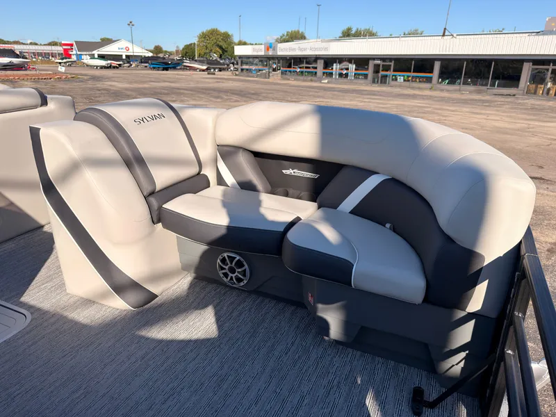 Slide: The Image of The image shows a luxurious, cushioned seating area on a Sylvan pontoon boat, surrounded by a parking lot. - 11