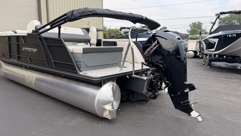 Slide: The Image of A 2027 Starcraft EX 20 Q DH pontoon boat with an outboard motor, parked on an asphalt lot. - 48