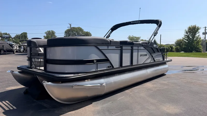 Slide: The Image of A modern pontoon boat with a gray and black design, parked on a lot under a blue sky. - 3