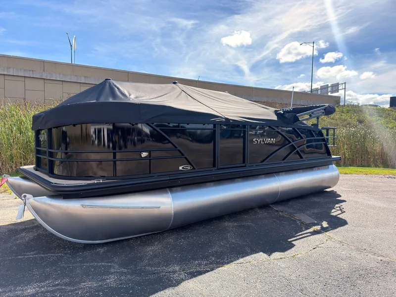 The Image of 2027 Sylvan Mirage 8520 CLZ DH pontoon boat with a black cover, parked on pavement. - 0