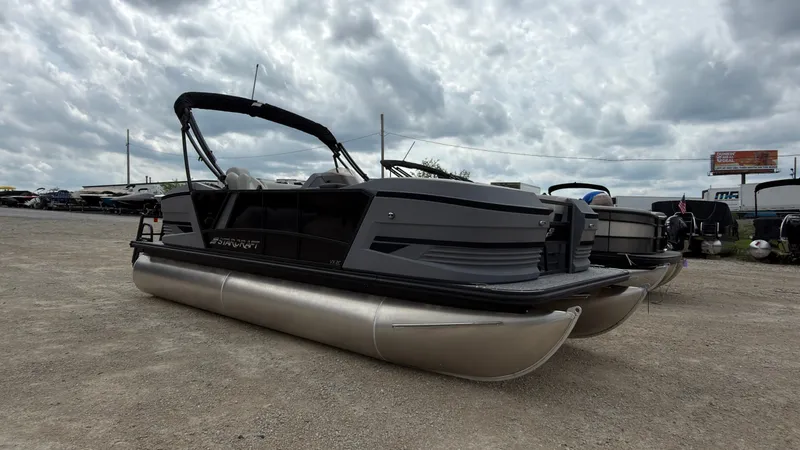 Slide: The Image of A gray pontoon boat by Starcraft, model VX 20 Q DH, sits on a gravel lot under cloudy skies. - 10