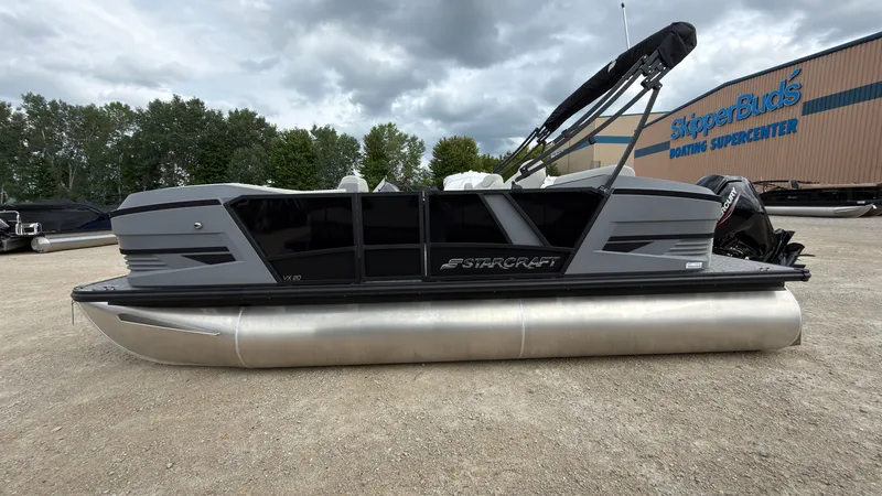Slide: The Image of A gray Starcraft VX 20 Q DH pontoon boat is parked on gravel in front of a building. - 1