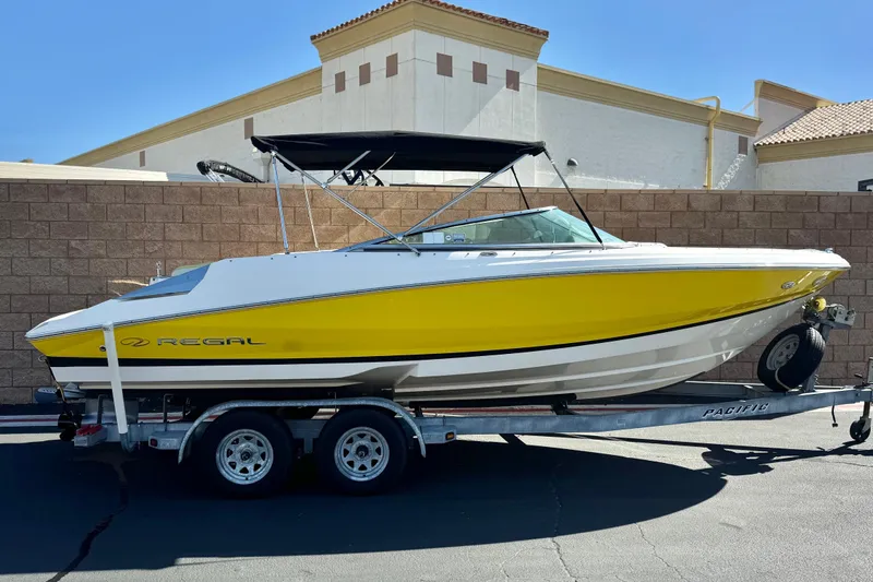 Slide: The Image of 2005 Regal 2200 Bowrider boat with yellow hull on a trailer, parked outdoors. - 0