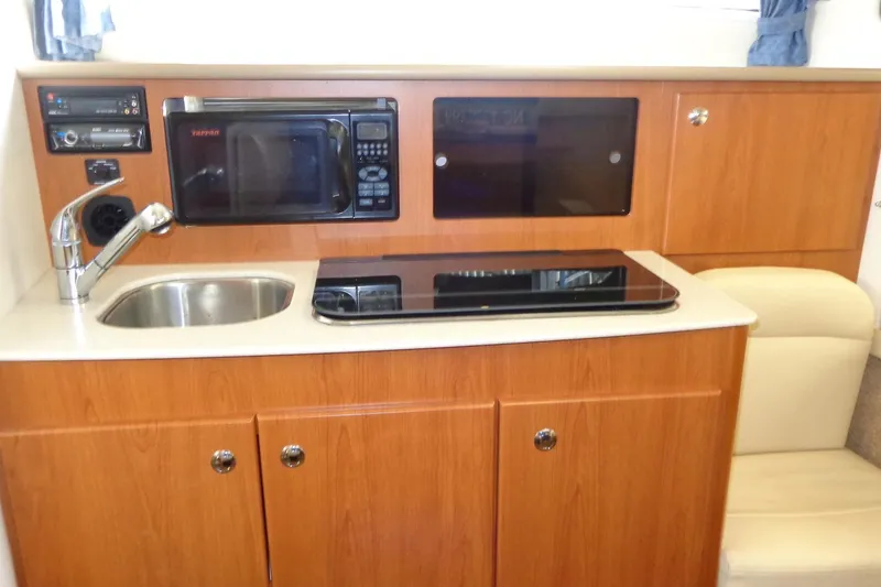 Slide: The Image of 2007 Bayliner 285 boat kitchen with sink, microwave, and stove in wooden cabinetry. - 25