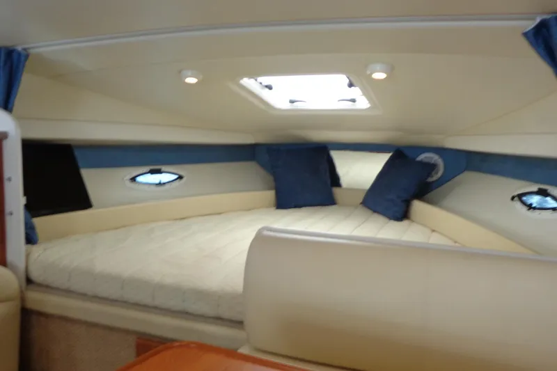 Slide: The Image of 2007 Bayliner 285 cabin interior with cozy bed, blue accents, and overhead lighting. - 26