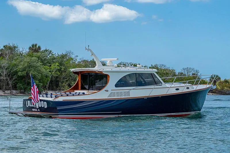 Slide: The Image of 2021 Hinckley Talaria 43 yacht cruising on a scenic waterway with lush greenery. - 2