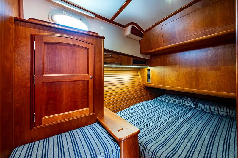 Slide: The Image of 2021 Hinckley Talaria 43 cabin interior with wooden finish and striped bedding. - 41