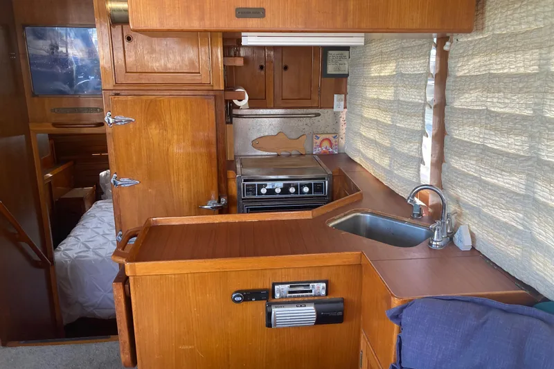 Slide: The Image of 1986 Island Gypsy 40 Motor Yacht interior with wooden cabinetry, compact kitchen, and cozy sleeping area. - 28