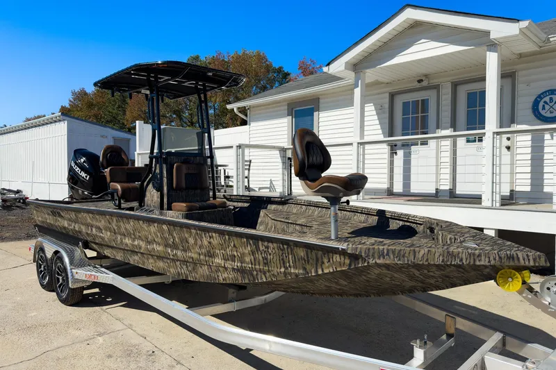 Slide: The Image of 2026 Excel Bay Pro Elite 220 boat on trailer, camo design, parked near white building. - 22
