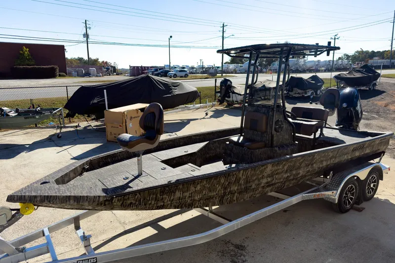 Slide: The Image of 2026 Excel Bay Pro Elite 220 boat on trailer, camo design, parked outdoors. - 23