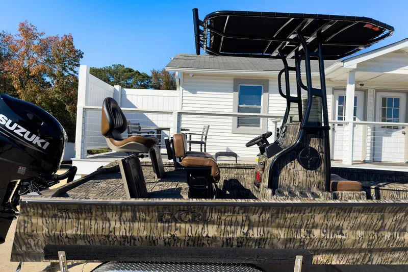 Slide: The Image of 2026 Excel Bay Pro Elite 220 boat with Suzuki engine, camo design, and seating, docked outdoors. - 27