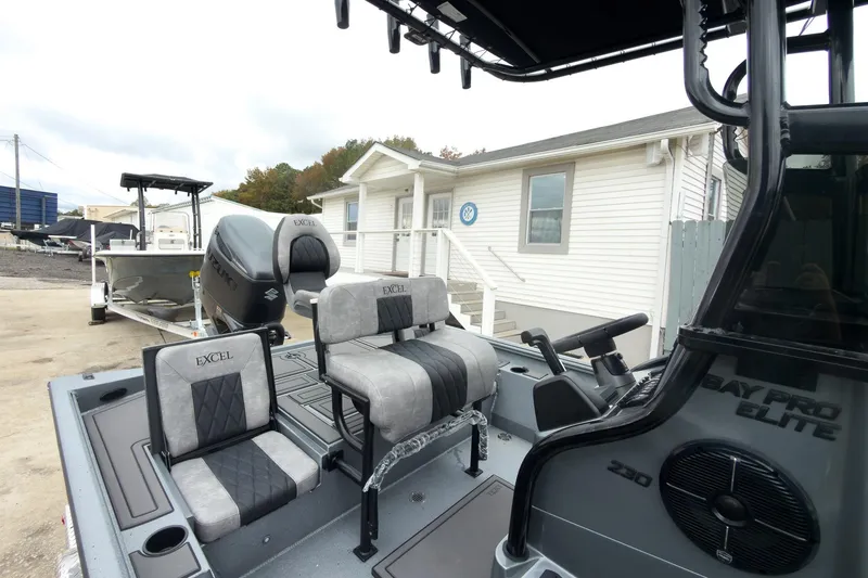 Slide: The Image of 2026 Excel Bay Pro Elite 230 boat with seating and motor, parked near a white building. - 17