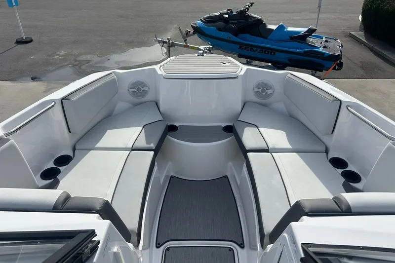 Slide: The Image of 2024 Yamaha Boats AR220 interior with spacious seating and cup holders, parked near a Sea-Doo. - 5