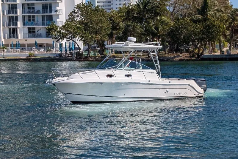 Slide: The Image of 2014 Robalo R305 Walkaround boat cruising on a sunny waterway near buildings and trees. - 2