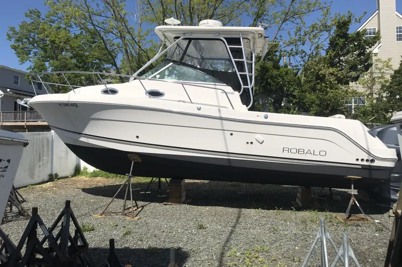 Slide: The Image of 2014 Robalo R305 Walkaround boat on stands, outdoors, surrounded by trees and buildings. - 6