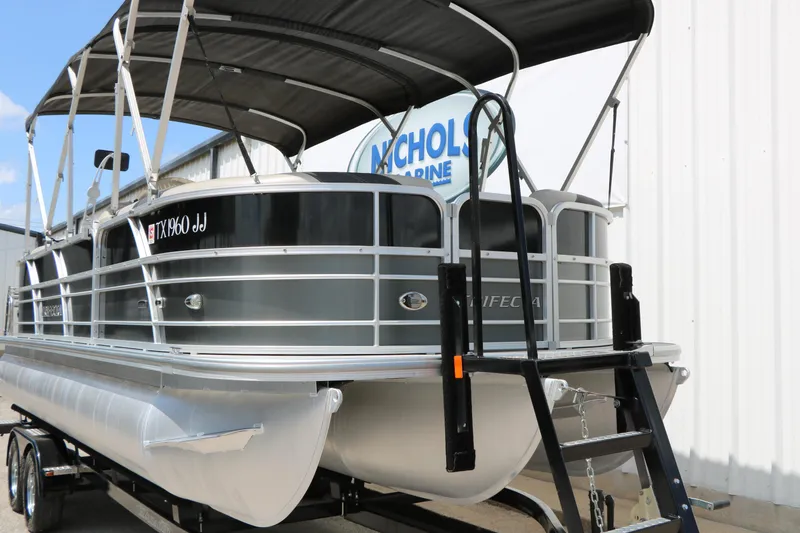 Slide: The Image of 2020 Trifecta 24RF LE pontoon boat with canopy on trailer, parked near building. - 3