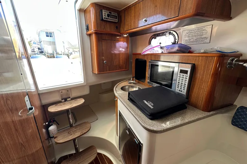 Slide: The Image of 2007 Pursuit OS 285 Offshore cabin interior with kitchenette, microwave, and wooden cabinetry. - 13