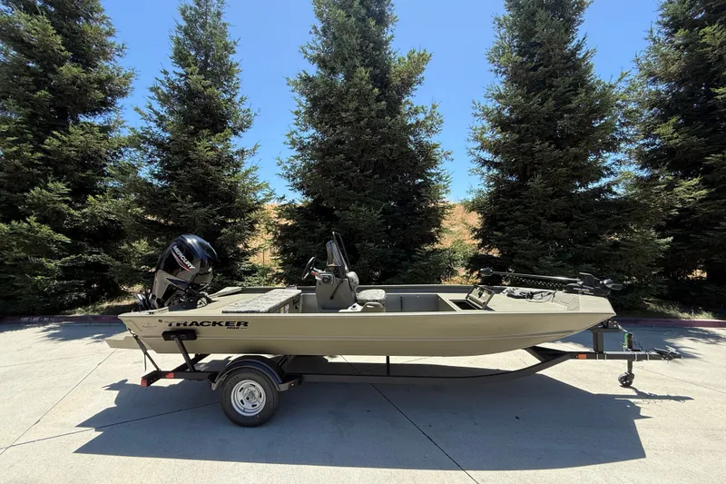 The Image of 2026 Tracker Grizzly 1860 CC boat on trailer, surrounded by tall trees. - 0