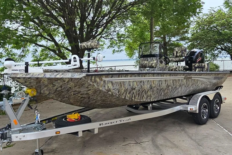 The Image of 2026 Ranger RB200 boat with camouflage design on a trailer, parked near a lake. - 0