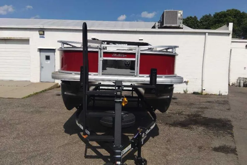Slide: The Image of 2026 Sun Tracker Bass Buggy 18 DLX pontoon boat on trailer, parked outside a building. - 3