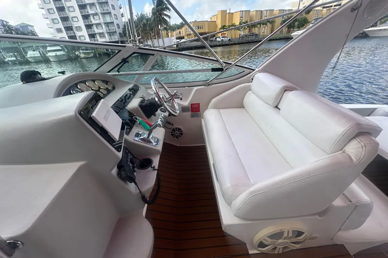 Slide: The Image of 2001 Sea Ray 340 Sundancer cockpit with white seating and steering wheel, docked by waterfront buildings. - 23