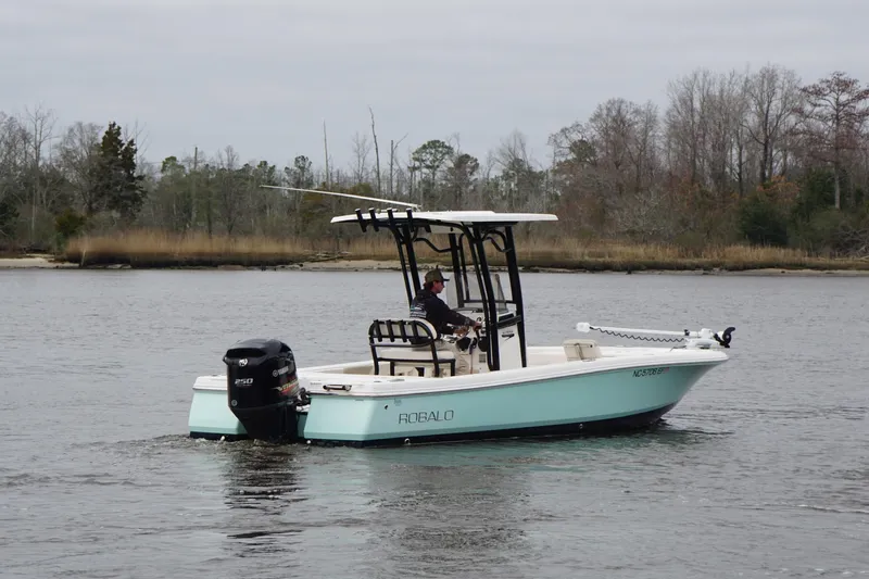 Slide: The Image of 2017 Robalo 246 Cayman boat cruising on a calm lake with trees in the background. - 18