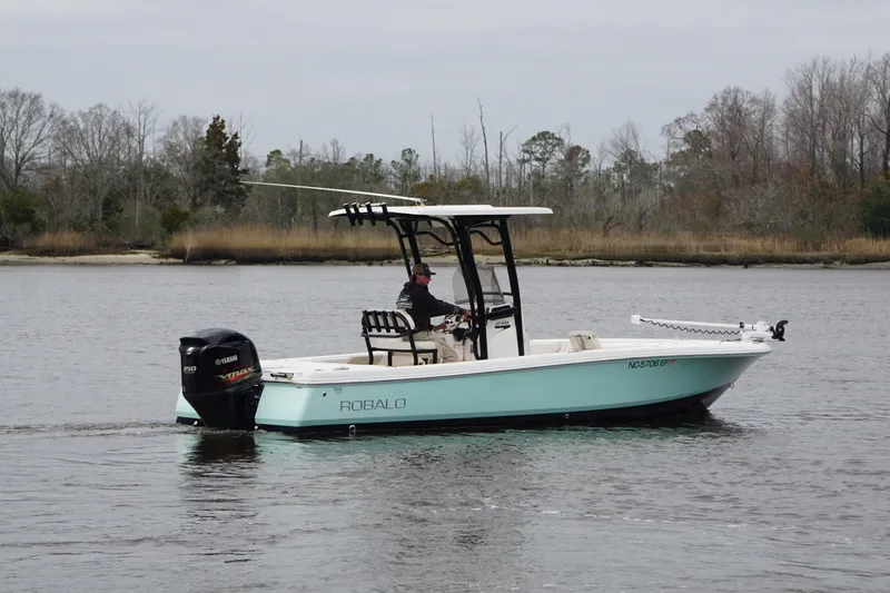 Slide: The Image of 2017 Robalo 246 Cayman boat cruising on a calm lake with trees in the background. - 4