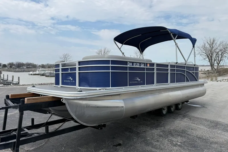Slide: The Image of 2023 Bennington 24SSRC pontoon boat with blue canopy on a trailer by the water. - 13