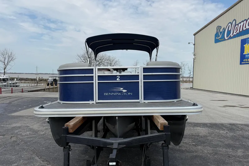 Slide: The Image of 2023 Bennington 24SSRC pontoon boat on trailer, parked near a building. - 2