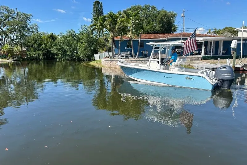 Slide: The Image of 2018 Sea Hunt Ultra 225 boat on calm water near a house with trees. - 19