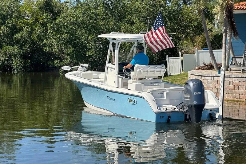 Slide: The Image of 2018 Sea Hunt Ultra 225 boat with American flag, cruising on a calm waterway. - 20
