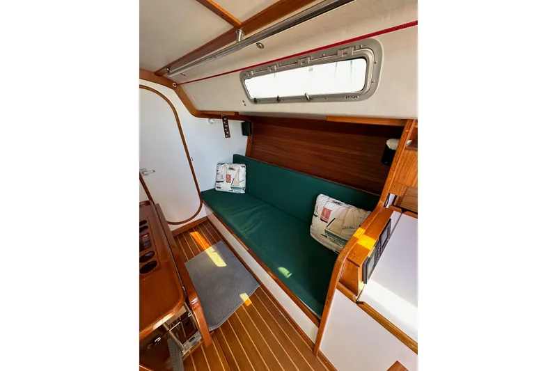 Slide: The Image of 1996 J Boats J/120 interior with green cushioned seating, wooden accents, and nautical-themed pillows. - 59