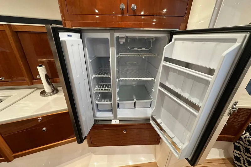 Slide: The Image of Open refrigerator inside 2020 Intrepid 475 Sport Yacht, showcasing spacious interior and wooden cabinetry. - 4