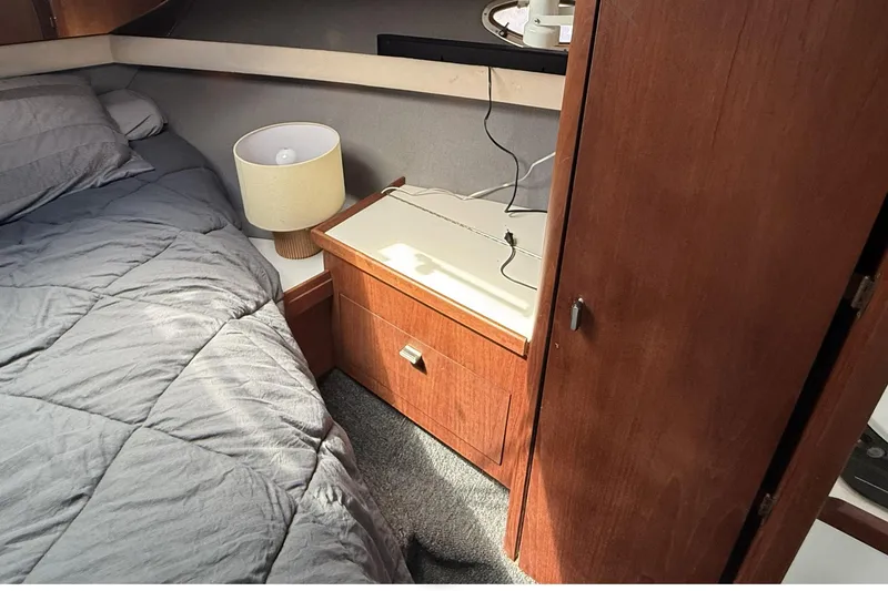 Slide: The Image of 1989 Tiara Yachts 3100 Flybridge cabin interior with bed, lamp, and wooden cabinet. - 26