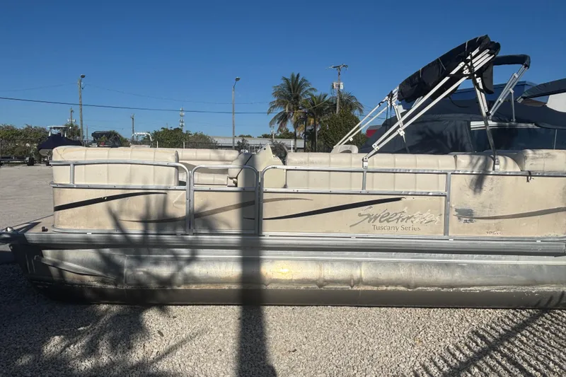 Slide: The Image of Pontoon boat Sweetwater 1880 C 2007 model, parked on gravel under clear blue sky. - 2