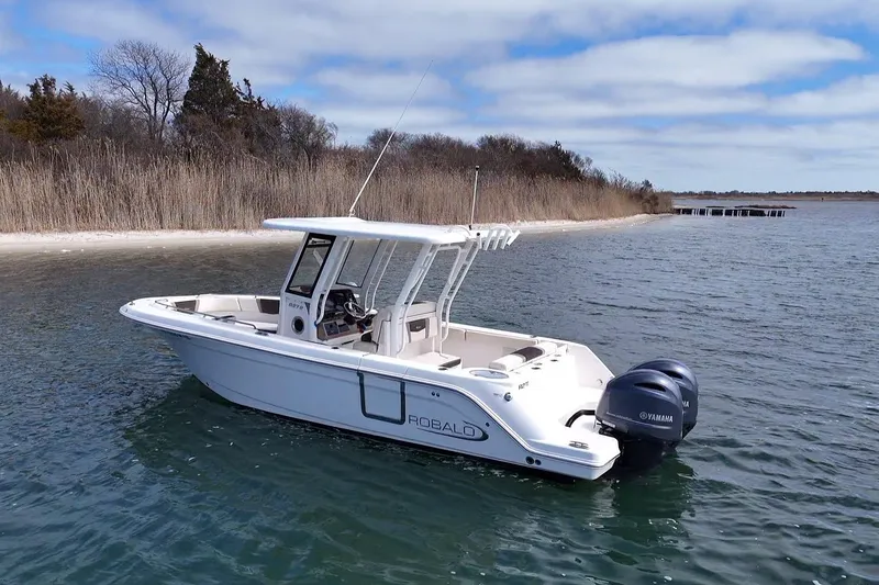 Slide: The Image of 2020 Robalo R272 Center Console boat on calm water near a shoreline. - 6