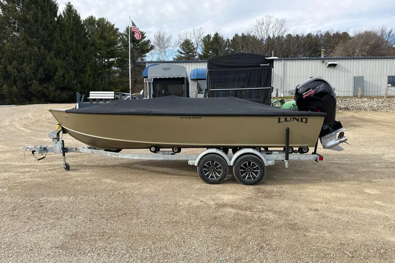 Slide: The Image of 2026 Lund 2075 Alaskan SS boat on trailer, parked outdoors with cover and outboard motor. - 13