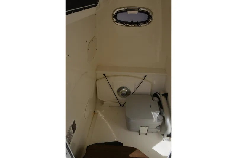 Slide: The Image of 2021 Boston Whaler 270 Dauntless interior cabin with portable toilet and porthole window. - 20