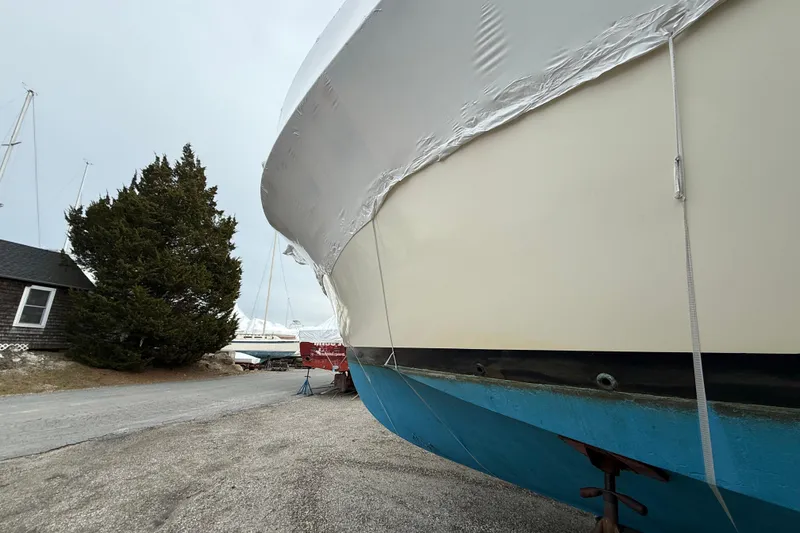 Slide: The Image of 1979 Hatteras 46 Convertible boat, wrapped and stored outdoors, near trees and a building. - 12