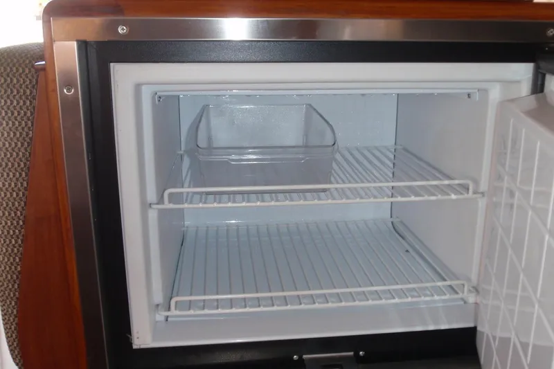 Slide: The Image of Empty refrigerator inside a 1985 Ocean Alexander boat, featuring wire shelves and a clear drawer. - 53