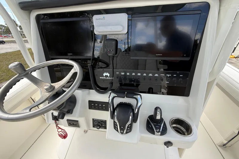 Slide: The Image of 2024 World Cat 295 CC boat dashboard with steering wheel, controls, and Garmin displays. - 14