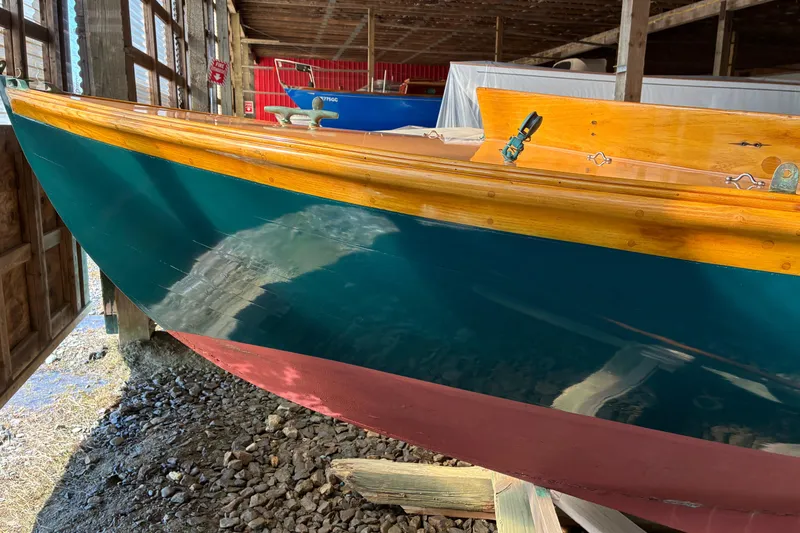 Slide: The Image of 1982 Herreshoff 12.5 footer sailboat with vibrant teal and red hull in a wooden shed. - 32