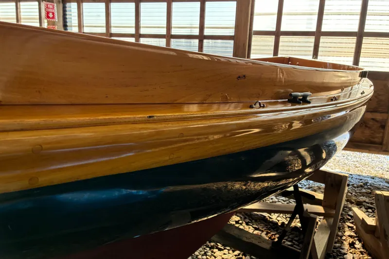 Slide: The Image of 1982 Herreshoff 12.5 footer sailboat with polished wooden hull in a sunlit boathouse. - 35