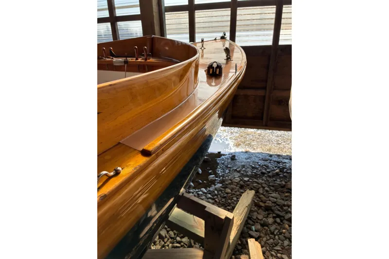 Slide: The Image of 1982 Herreshoff 12.5 footer sailboat with polished wooden deck in a boathouse. - 36