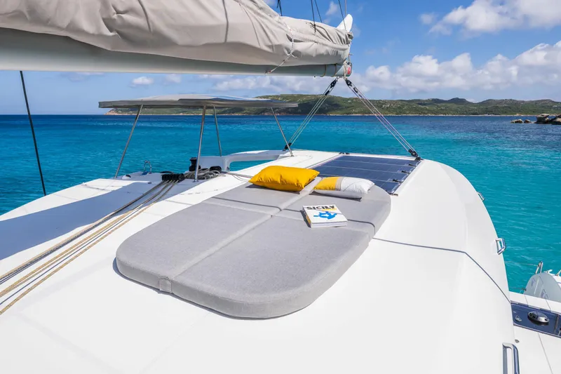 Slide: The Image of 2025 Lagoon 38 catamaran with sunbathing area, cushions, and book, anchored in turquoise waters. - 10