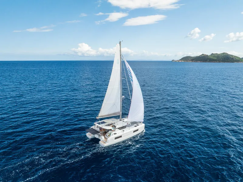 Slide: The Image of 2025 Lagoon 38 catamaran sailing on open sea with distant island view. - 62