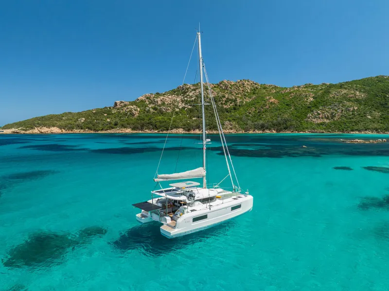 Slide: The Image of 2025 Lagoon 38 catamaran sailing in clear turquoise waters near a lush green island. - 68