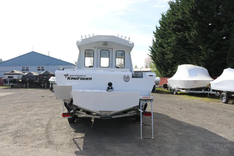Slide: The Image of 2026 KingFisher 2425 Escape HT boat, rear view, parked outdoors with covered boats nearby. - 3
